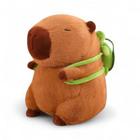 Kuscheltier Capybara, braun, mit grünem Schildkröten-Rucksack, sitzend auf weißem Hintergrund.