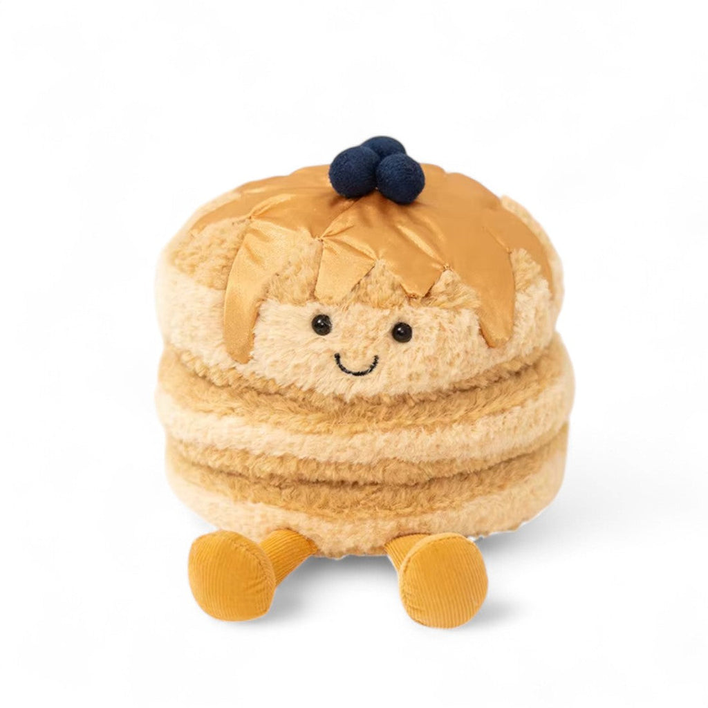 Pancakes Kuscheltier beige mit lächelndem Gesicht, gelben Beinchen und kleinen blauen Blaubeeren obenauf, sitzend auf weißem Hintergrund