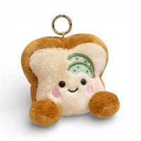 Ein kleiner Plüsch Schlüsselanhänger in Form einer beigen Toastscheibe mit grünem Gurkenbelag obenauf, lächelndes Gesicht mit großen runden Augen und rosa Wangen, kleinen braunen Pfötchen an beiden Seiten, Metallring zur Befestigung, auf weißem Hintergrund.