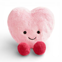 Ein weiches, flauschiges Kuscheltier in Herzform in Rosa, mit einem großen fröhlichen Lächeln, zwei runden glänzenden schwarzen Augen und zwei kleinen roten gestrickten Stoffpfötchen unten, auf einheitlich weißem Hintergrund