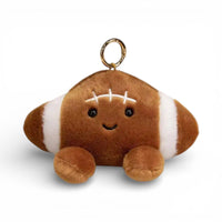 Kawaii-Kuscheltier in Form eines American-Football-Balls, 12 cm, strukturiertes braunes Leder mit weißen Streifen und Nähten, große glänzende schwarze Augen, fröhliches Lächeln, rosa Wangen, zwei pummelige braune Pfötchen unten, goldener Ring obenauf befestigt, auf weißem Hintergrund.